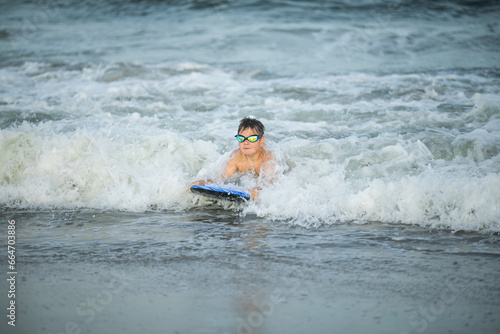 Little surfer learn to ride on surfboard on sea wave. Kid play in summer ocean, learning surfing, riding a wave. Little boy swim on kids surf board © Maria