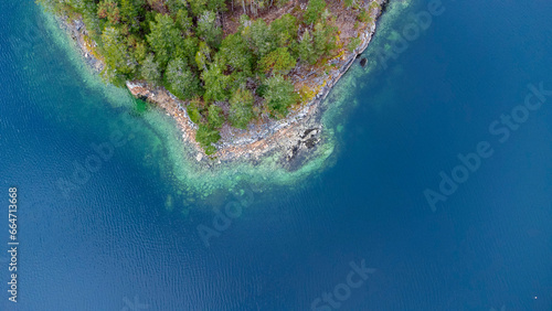 Edge of an island in the ocean. Trees cover the rocky surface. 