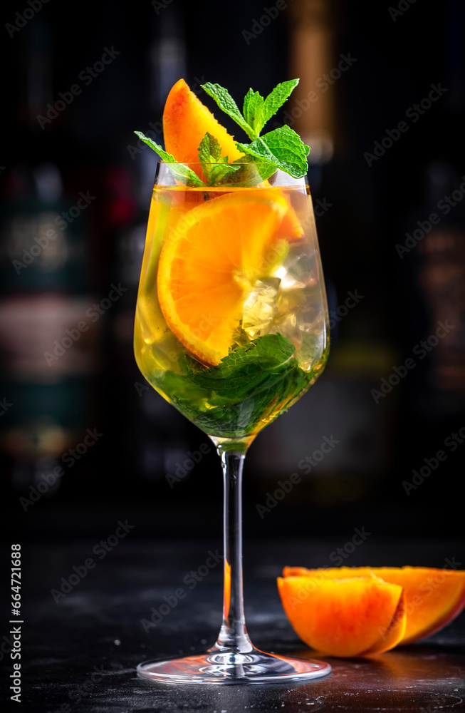 White sangria alcoholic cocktail drink with viura spanish wine, peach, orange, lime and ice. Black bar counter background, steel bar tools and bottles White sangria alcoholic cocktail drink with viura spanish wine, peach, orange, lime and ice. Black bar counter background, steel bar tools and bottles