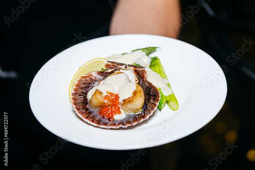 Grilled scallops in a shell with red caviar and asparagus under a sauce, luxury catering