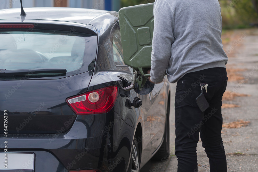 Ein Mann füllt mit einem Benzinkanister den Tank seines Autos mit Benzin nach Ein Mann füllt mit einem Benzinkanister den Tank seines Autos mit Benzin nach