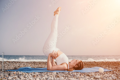 Woman sea yoga. Well looking middle aged woman with braids dreadlocks in white leggings and tops doing stretching pilates on yoga mat near sea. Female fitness yoga routine concept. Healthy lifestyle.