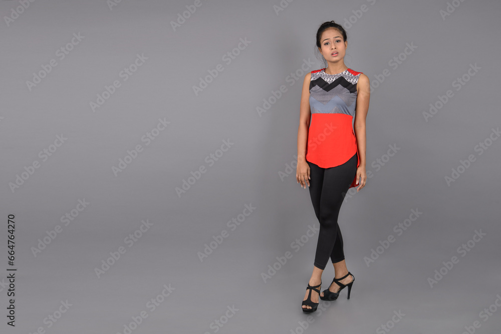 Fototapeta premium Studio shot of a young, beautiful Indian female model in casual wear wearing red and grey designer top and black jeans against white background. Female model. Fashion Portrait.