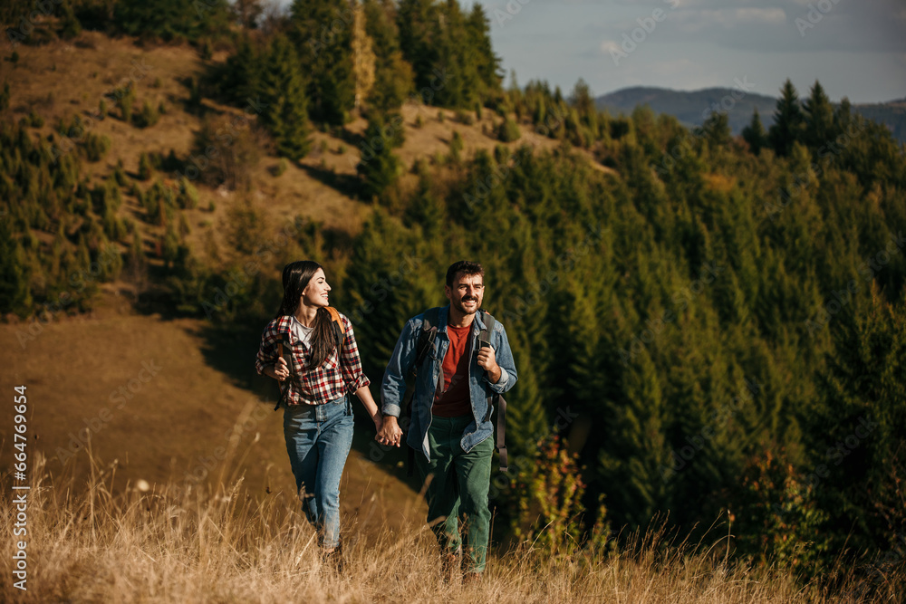 A diverse couple with radiant smiles embarking on an adventurous hike, carrying vibrant backpacks on a sun-drenched day A diverse couple with radiant smiles embarking on an adventurous hike, carrying vibrant backpacks on a sun-drenched day