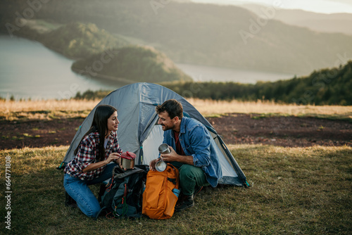 Loving pair embraces the great outdoors as they set up camp on a scenic hillside  basking in the breathtaking view of a distant glistening lake