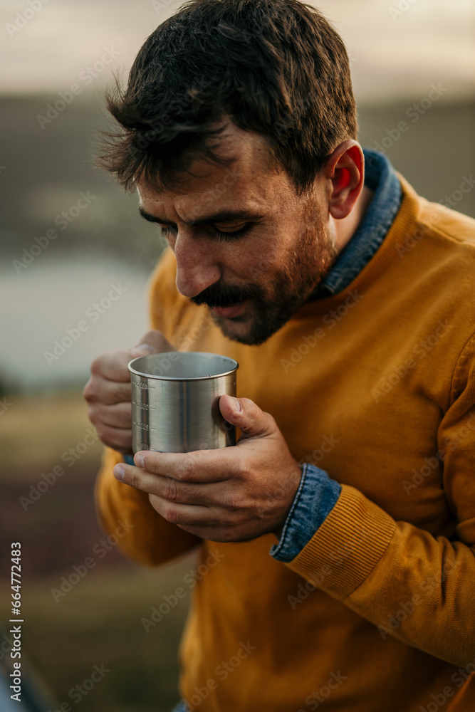 Pensive caucasian man enjoying a hot drink during a camping in the nature. Pensive caucasian man enjoying a hot drink during a camping in the nature.