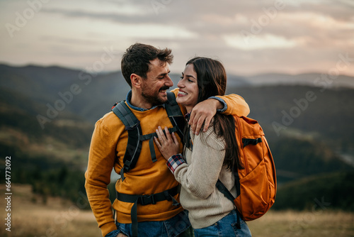 Two friends walking uphill with backpacks, catching sight of a serene lake