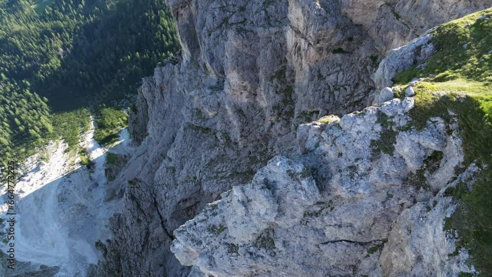 A vertical perspective showcases the Dolomites' sheer rock faces and rugged terrain, contrasting with patches of greenery and the tree-covered valley below. A vertical perspective showcases the Dolomites' sheer rock faces and rugged terrain, contrasting with patches of greenery and the tree-covered valley below.