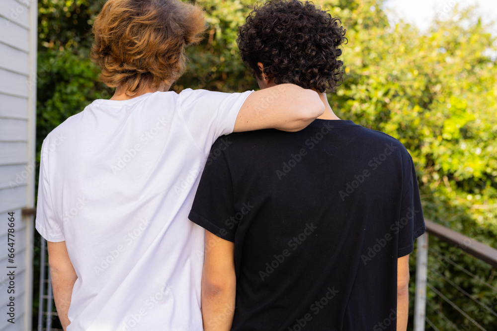 Rear view of two caucasian men wearing white and black short sleeved t shirts on balcony, copy space Rear view of two caucasian men wearing white and black short sleeved t shirts on balcony, copy space
