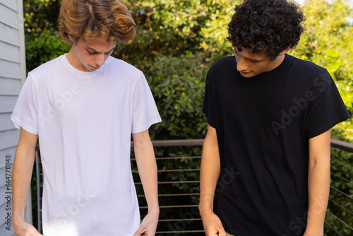 Two caucasian men wearing white and black short sleeved t shirts on balcony with copy space