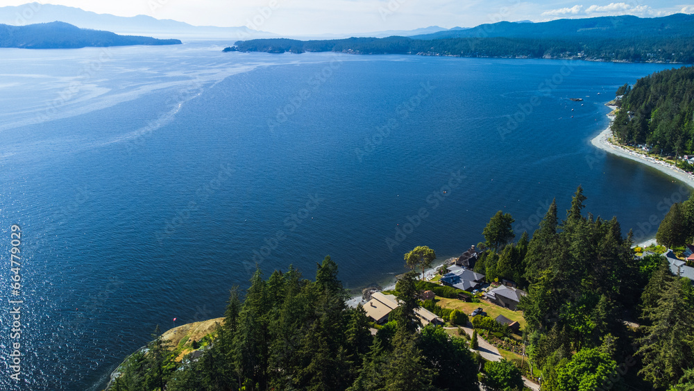 Halfmoon Bay, Sunshine Coast with Thormanby island in the distance. Forest stretches along the coastline with a few homes poking out from the trees. Halfmoon Bay, Sunshine Coast with Thormanby island in the distance. Forest stretches along the coastline with a few homes poking out from the trees.