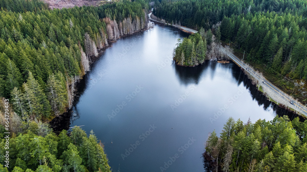 Lake in the forest next to a highway. Trees surround the lake's shore. 
