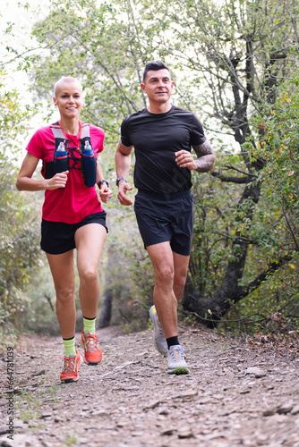 Fototapeta Naklejka Na Ścianę i Meble -  vertical photo of a couple practicing trail running in the forest, concept of sport in nature and healthy lifestyle, copy space for text
