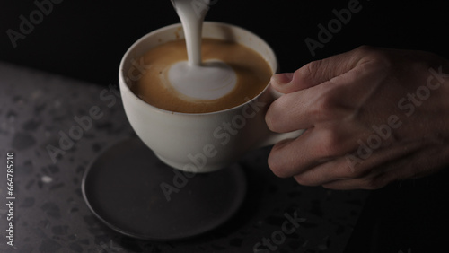 Making cappuccino, pour steamed milk into white cup with espresso
