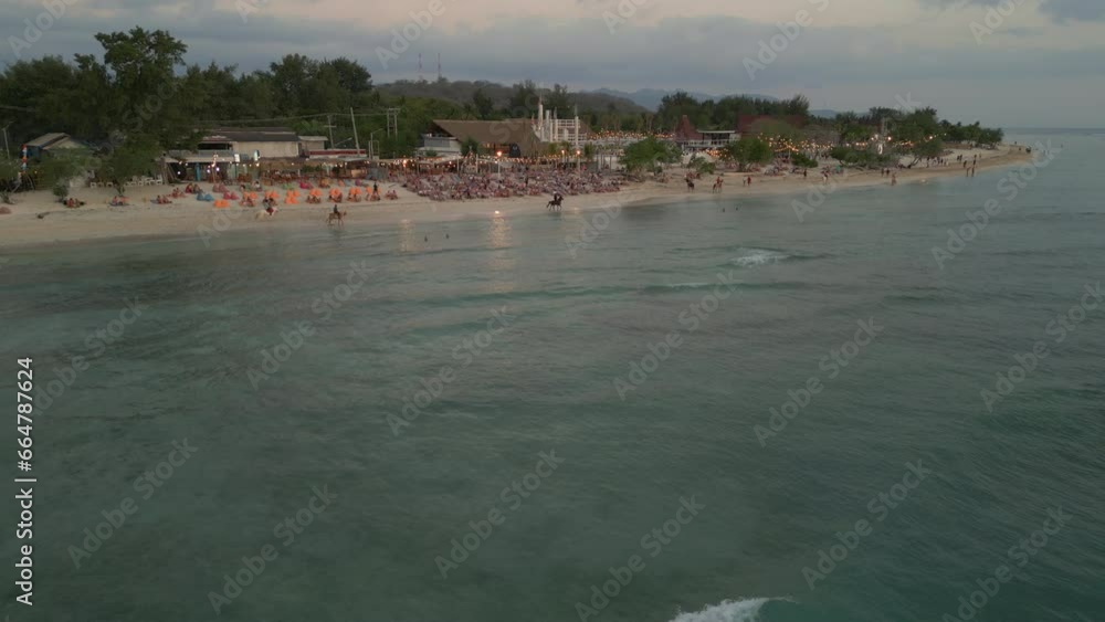 Drone shot moving over sea towards busy beach and horse riding on Gili Trawangan island in Bali Drone shot moving over sea towards busy beach and horse riding on Gili Trawangan island in Bali