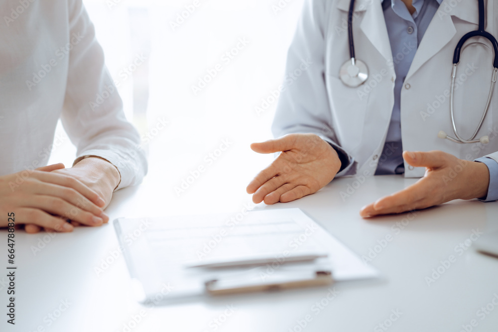 Doctor and patient discussing current health questions while sitting near of each other and using clipboard at the table in clinic, just hands closeup. Medicine concept Doctor and patient discussing current health questions while sitting near of each other and using clipboard at the table in clinic, just hands closeup. Medicine concept