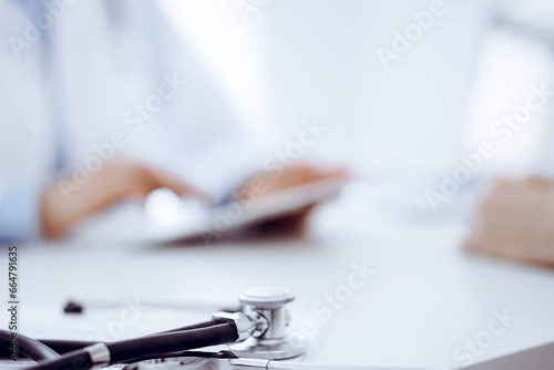 Stethoscope lying on the tablet computer in front of a doctor and patient sitting opposite each other and using tablet computer at the background . Medicine, healthcare concept