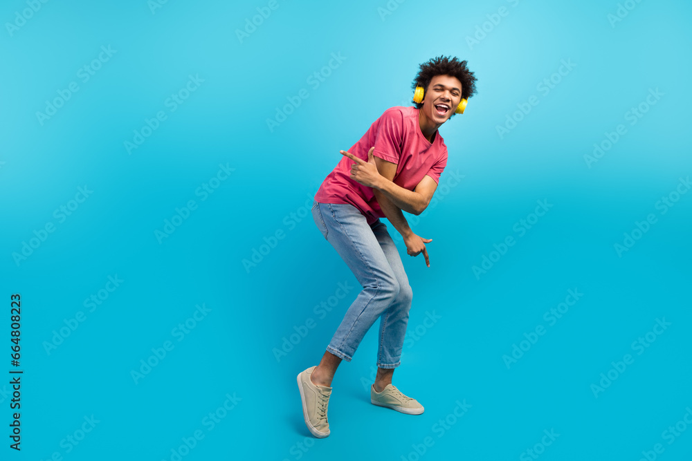 Full size photo of attractive young man dancing yellow headphones sing song wear trendy pink clothes isolated on blue color background