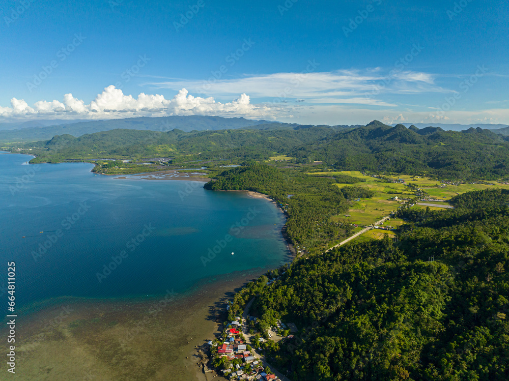 Tropical landscape of coastline with small village and blue sea. Skyscape. Mindanao, Philippines.