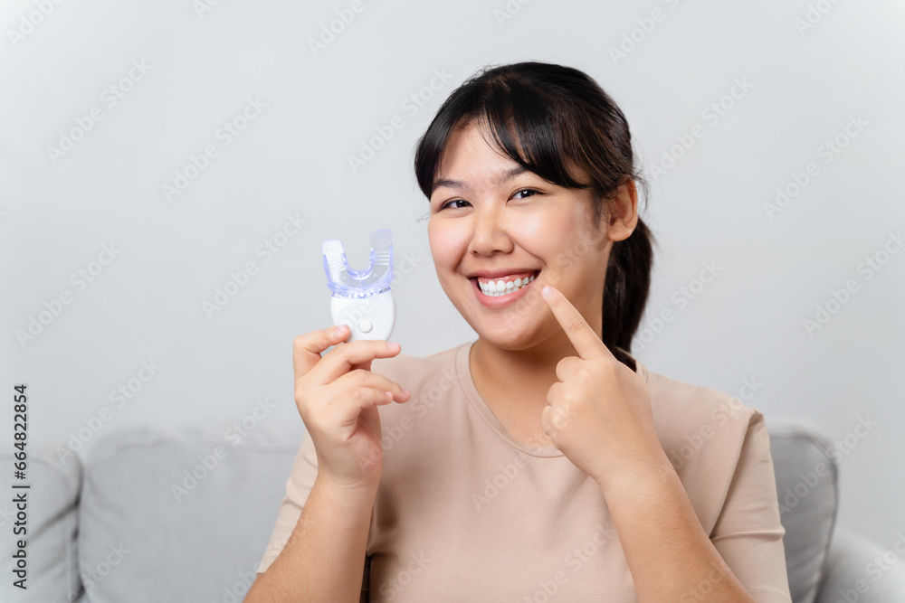 The woman is whitening her teeth with a teeth whitening device by herself in the living room at home. Health and medical concept. The woman is whitening her teeth with a teeth whitening device by herself in the living room at home. Health and medical concept.