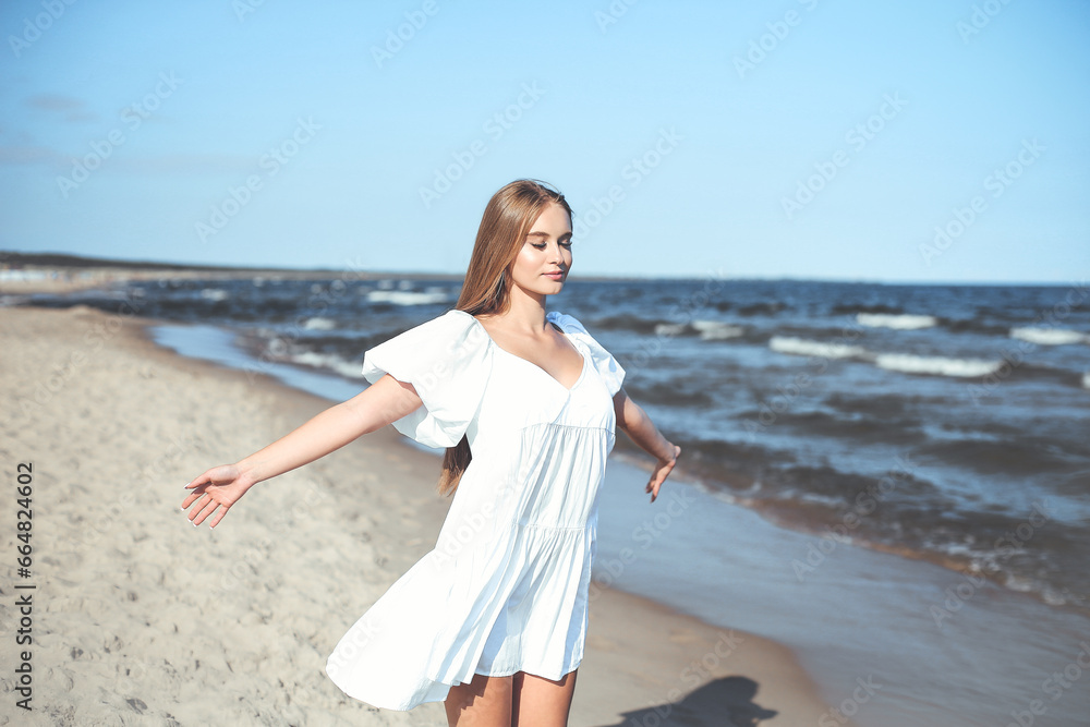 Happy smiling beautiful woman is on the ocean beach in a white summer dress, open arms Happy smiling beautiful woman is on the ocean beach in a white summer dress, open arms