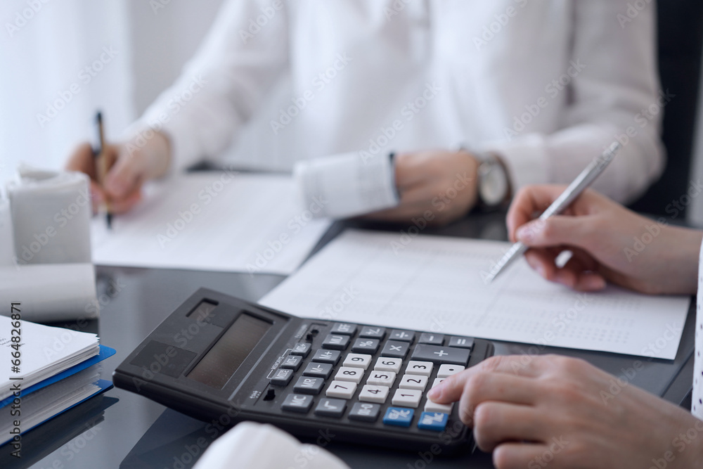 Two accountants use a calculator and laptop computer for counting taxes or revenue balance. Business, audit, and taxes concepts Two accountants use a calculator and laptop computer for counting taxes or revenue balance. Business, audit, and taxes concepts
