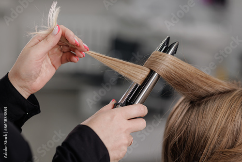 professional hairdresser curls hair with a curling iron in a beauty salon, hands of a hairdresser with a hair curling iron, close-up