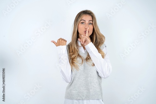 Young business woman wearing formal clothing asking to be quiet with finger on lips pointing with hand to the side. Silence and secret concept.