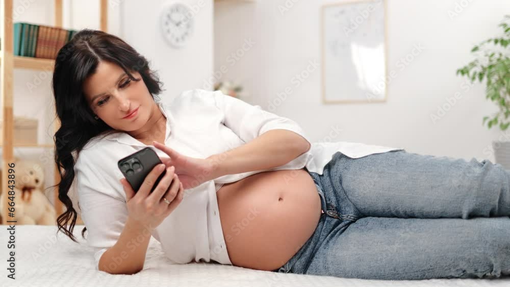 Relaxed pregnant woman future mother use smartphone searching information lying white carpet floor Relaxed pregnant woman future mother use smartphone searching information lying white carpet floor