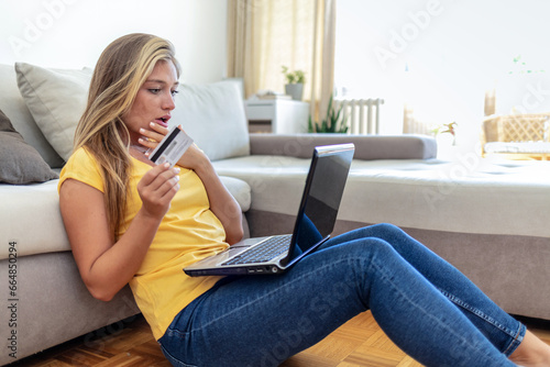 Shot of a focused young woman seated on the floor while doing online shopping on her computer in the living room at home.