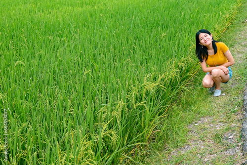 A girl pretends to be cute, and half squats in a green paddy field.