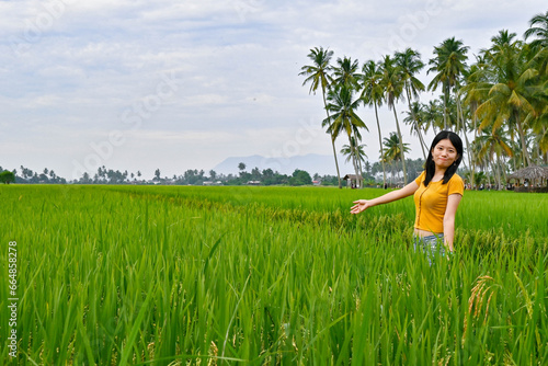 A girl stands with open hands in the endless green paddy field.
