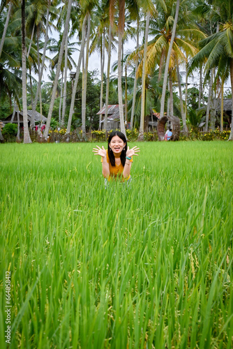 A girl pretends to be cute, and half squats in a green paddy field.