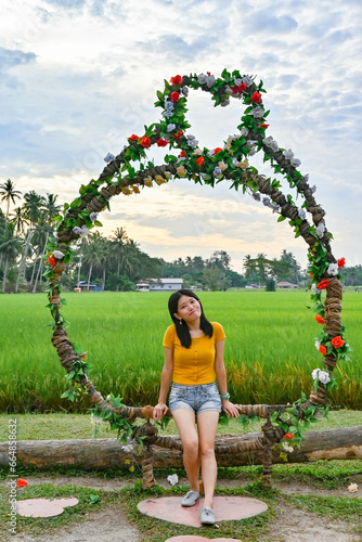 A girl sits on the garland beside the green paddy field.