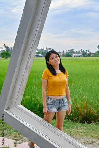 A girl stands in a frame beside the green paddy field.