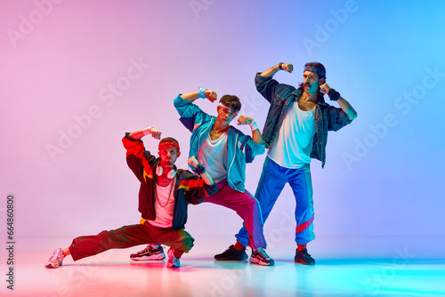 Funny image of three men in stylish, vintage sportswear training aerobics and gymnastics against gradient pink blue background in neon light. Concept of sportive and active lifestyle, retro style. Ad