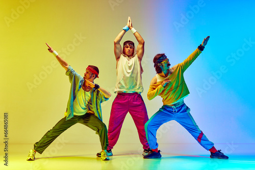 Fototapeta Naklejka Na Ścianę i Meble -  Stylish three men in colorful sportswear posing against gradient yellow blue background in neon light. Athletes. Concept of sportive and active lifestyle, humor, retro style. Ad