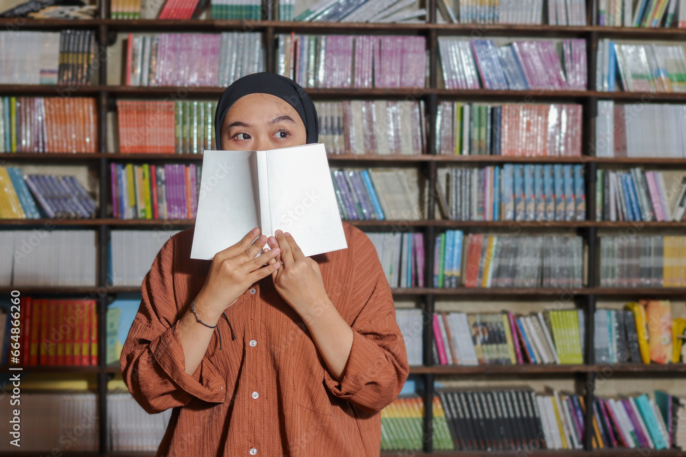 Portrait of Asian hijab woman covering her half head with a book in ...