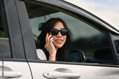 Charming millennial woman talking on mobile phone and looking on the road through the window