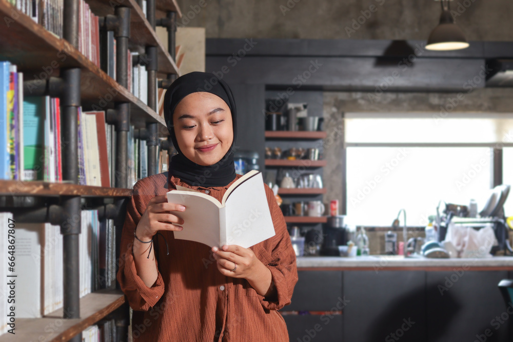 Portrait of Asian hijab woman holding book in front of library bookshelf. Muslim girl reading a book. Concept of literacy and knowledge Portrait of Asian hijab woman holding book in front of library bookshelf. Muslim girl reading a book. Concept of literacy and knowledge