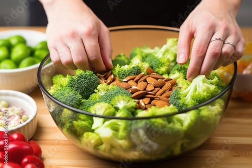 hand crushing almonds over a bowl of broccoli raisin salad