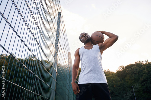View from below. Young black man is with basketball ball outdoors