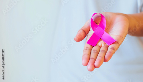 A woman's hand holds a pink ribbon symbolizing the fight against breast cancer