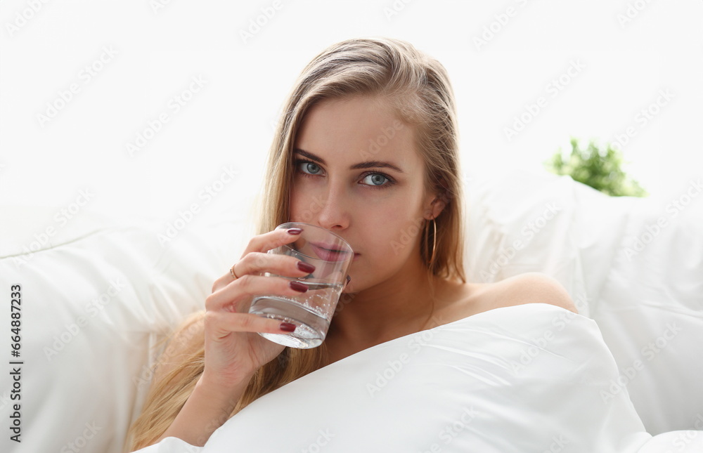 beautiful young blond woman hold glass of water in arm early morning stay in bed