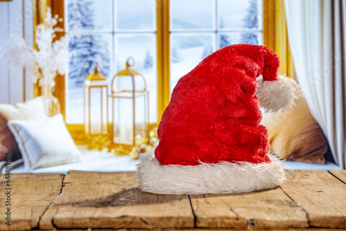 Red santa claus on wooden desk and winter window background in home interior. Cold december time and empty space for your products. 