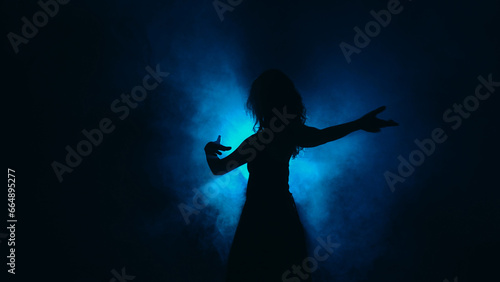 Silhouette dancing. Contemporary performance. Graceful flexibility. Tender slim woman moving in haze shadow spot light dark background copy space.