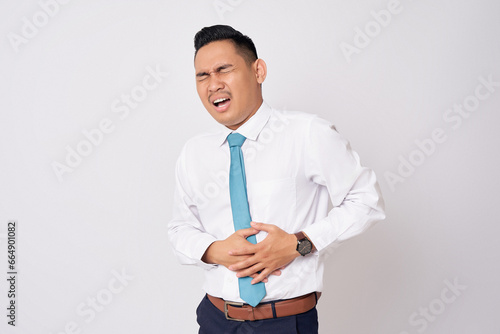 Abdominal Pain. Unhealthy young Asian businessman wearing formal shirt and tie suffering from stomachache isolated on white background