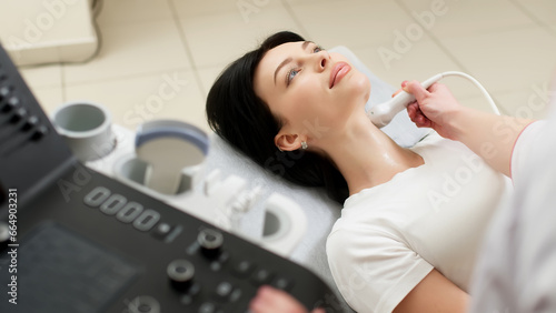 A doctor performs an ultrasound of the thyroid gland and cervical lymph nodes on a patient in a modern clinic against a light background. Advertising of modern medicine and technology photo
