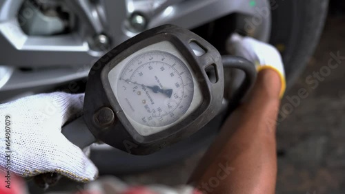 Mechanic wearing gloves checking tire pressure with the compressor at the service station, car repair. Professional tire fitting at car service