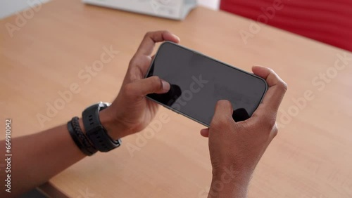 Mockup image of a hand using a mobile phone with a blank screen on a wooden table, playing a racing game online